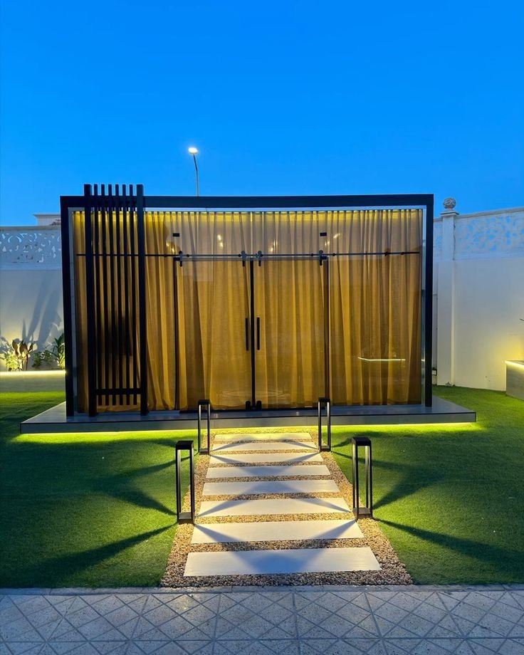 Black aluminium glass room with curtains and lit garden path at night
