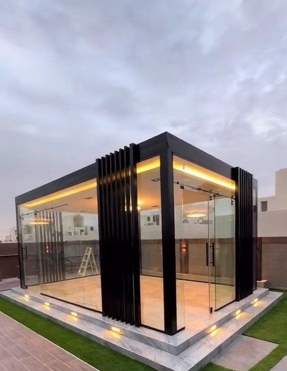 Glass room with black aluminium fins and warm LED lighting at dusk