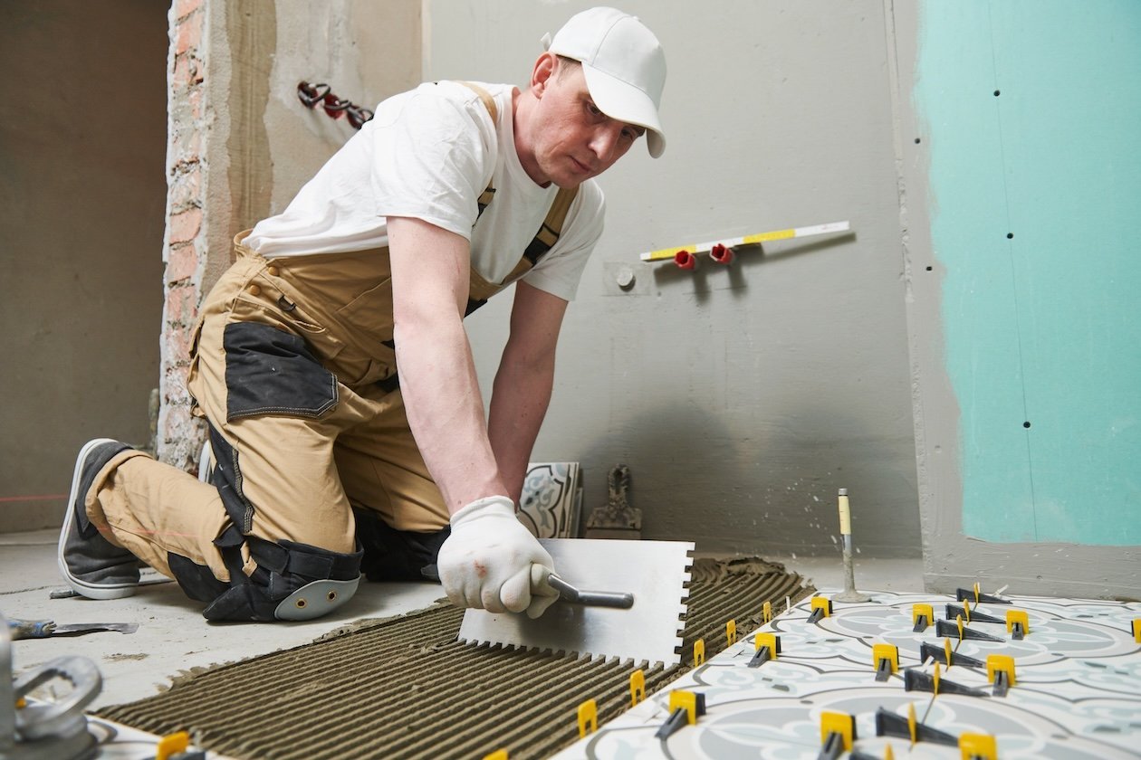 Installer laying floor tiles with adhesive